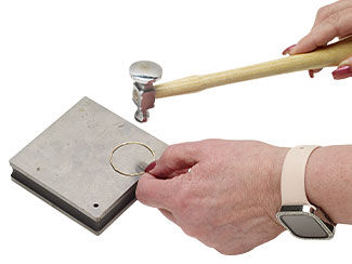 a hand hammering a circle of wire on a steel block